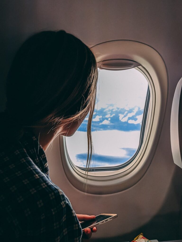Find out how family air travel has changed in the last few months.  As a girl looks out the airplane window and thinks about her flight.  Airplane Tips | Family Travel | Tips for Flying with Kids